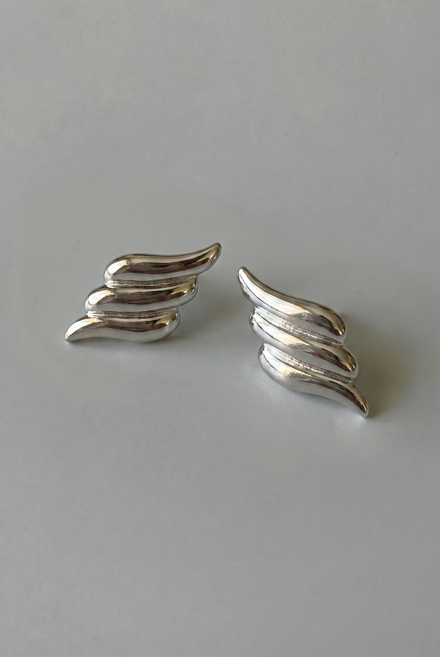 Pair of silver wing-shaped earrings on a gray background