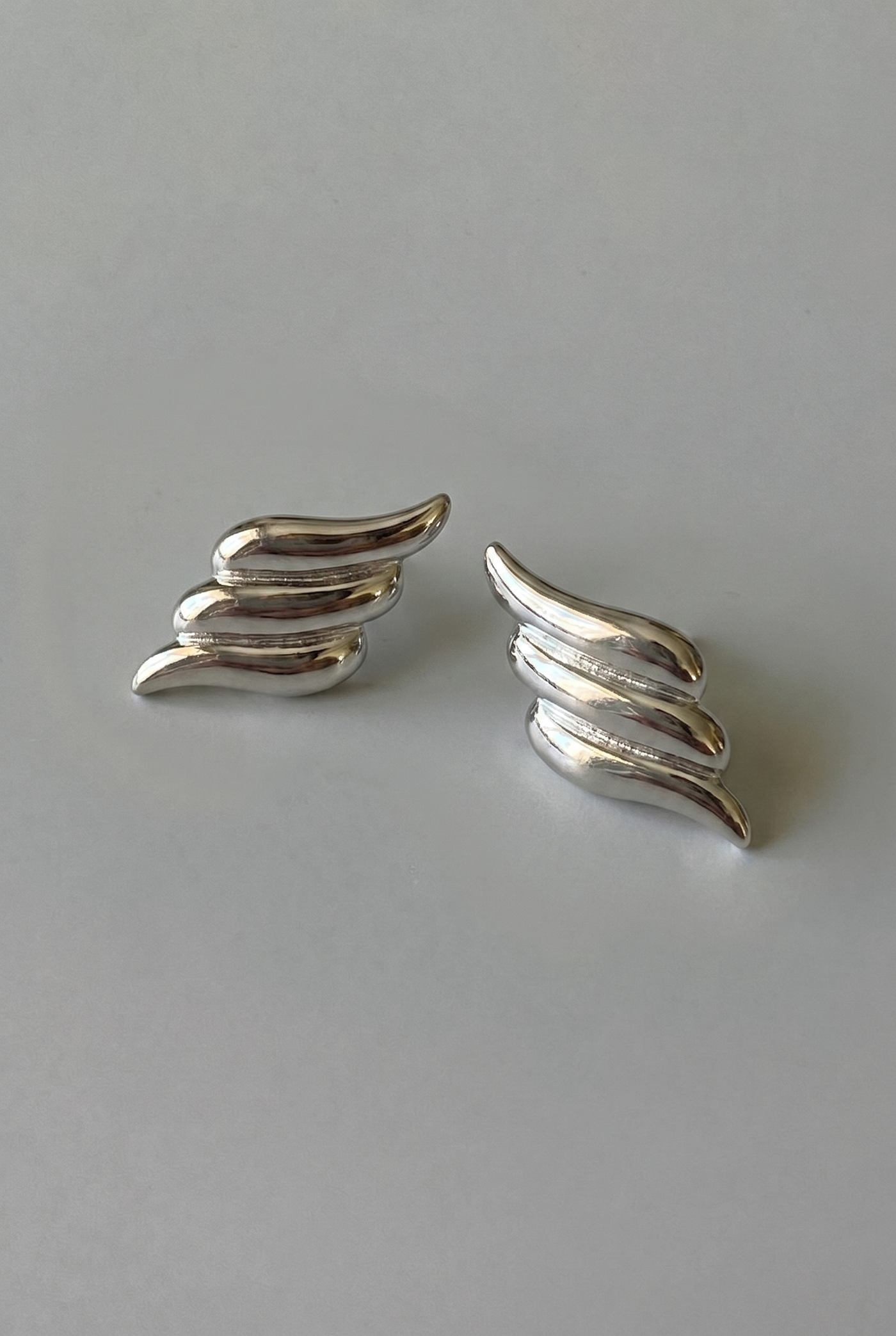 Pair of silver wing-shaped earrings on a gray background