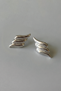 Pair of silver wing-shaped earrings on a gray background
