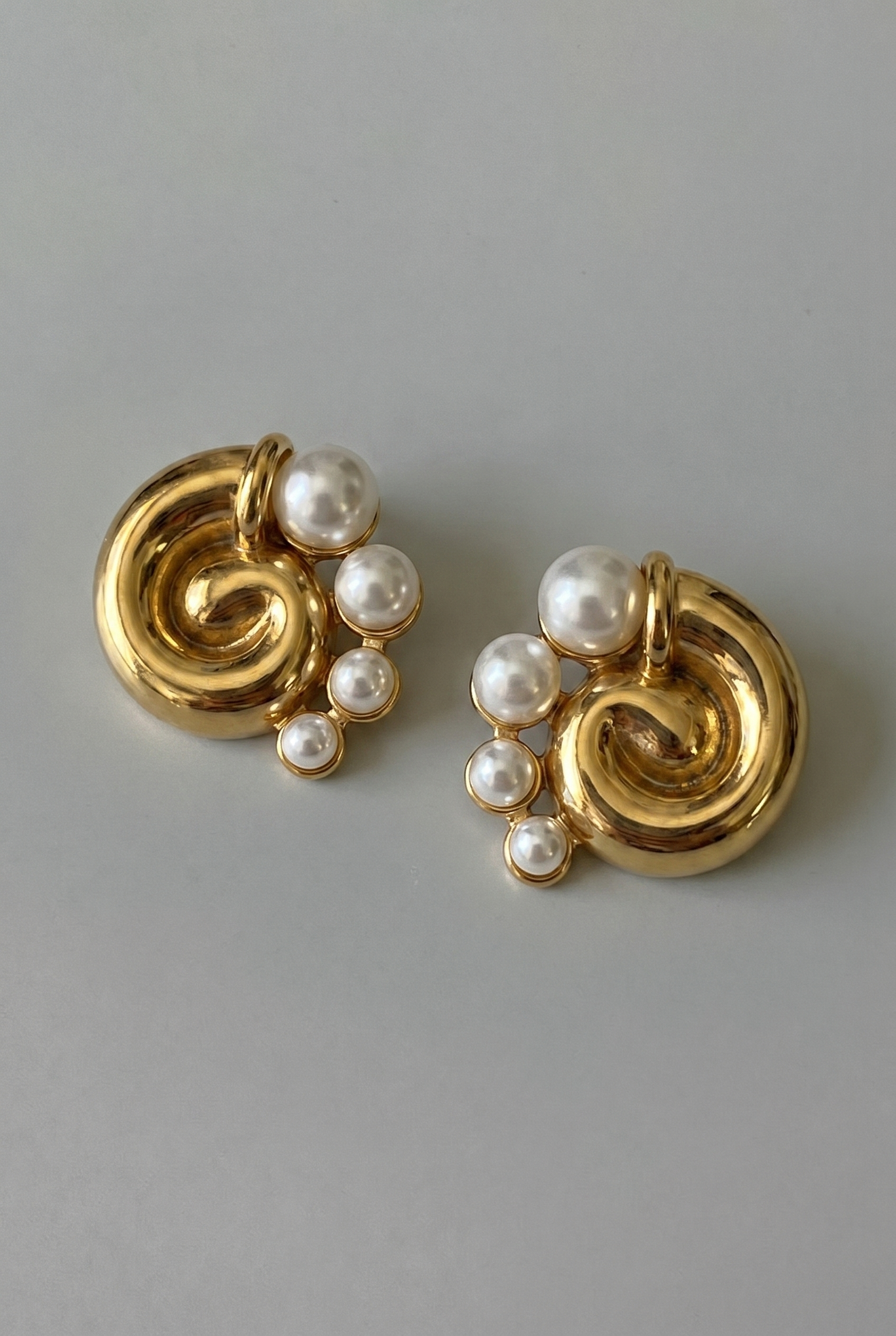 Gold earrings with pearl beads on a gray background