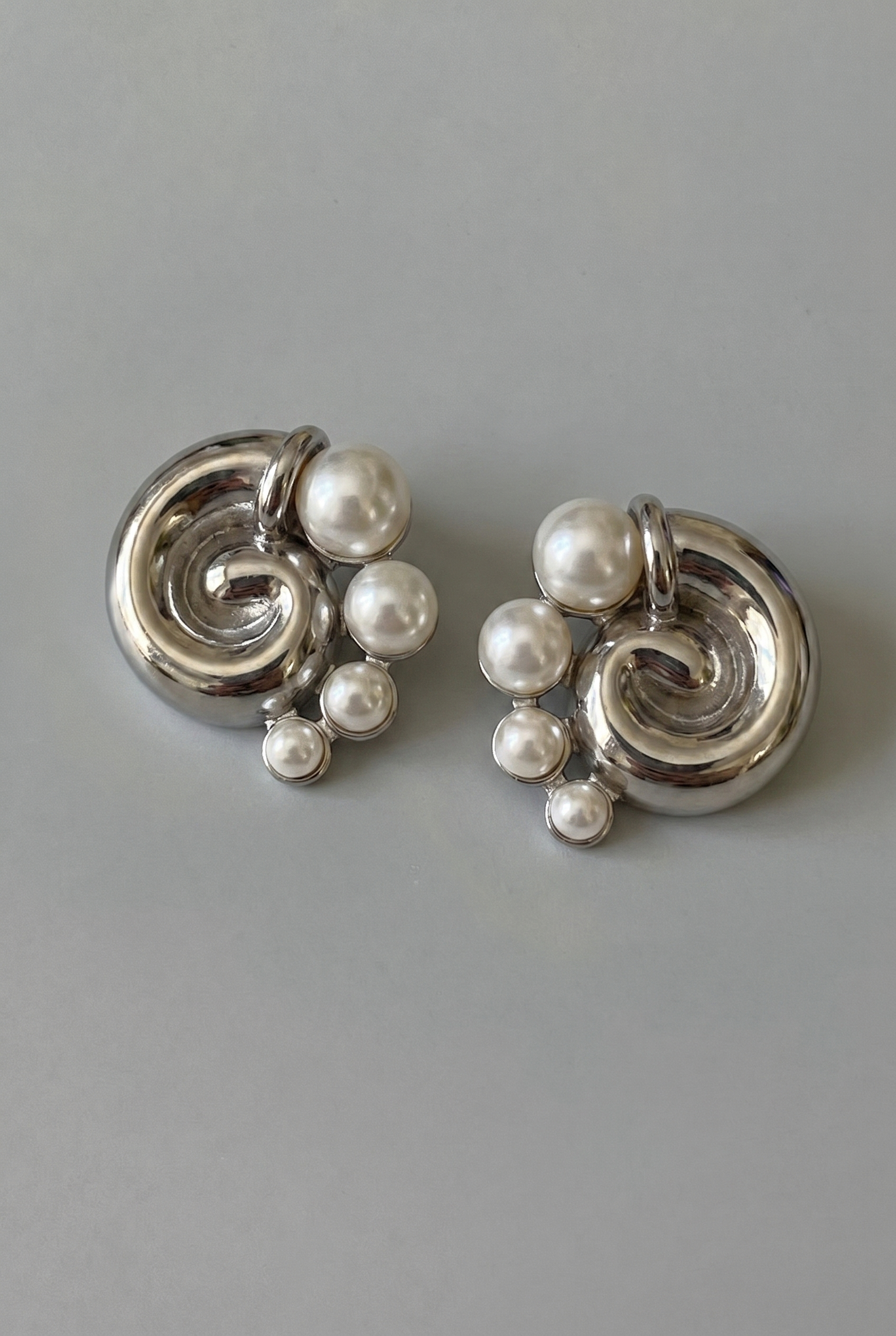Silver earrings with pearl-like beads on a gray background