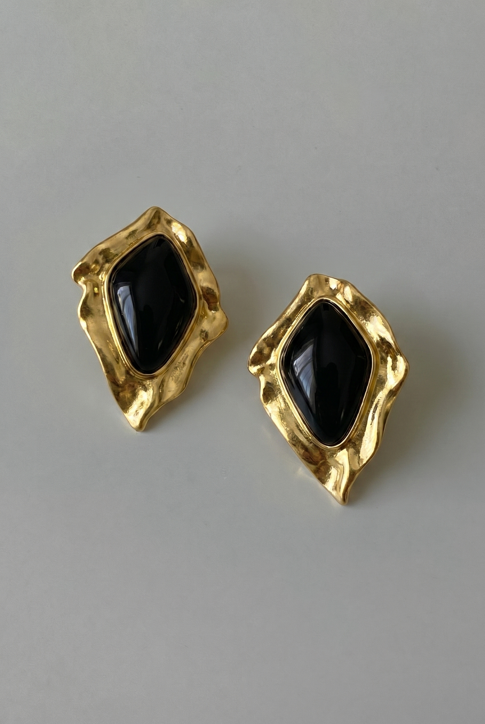 Gold earrings with black gemstones on a gray background
