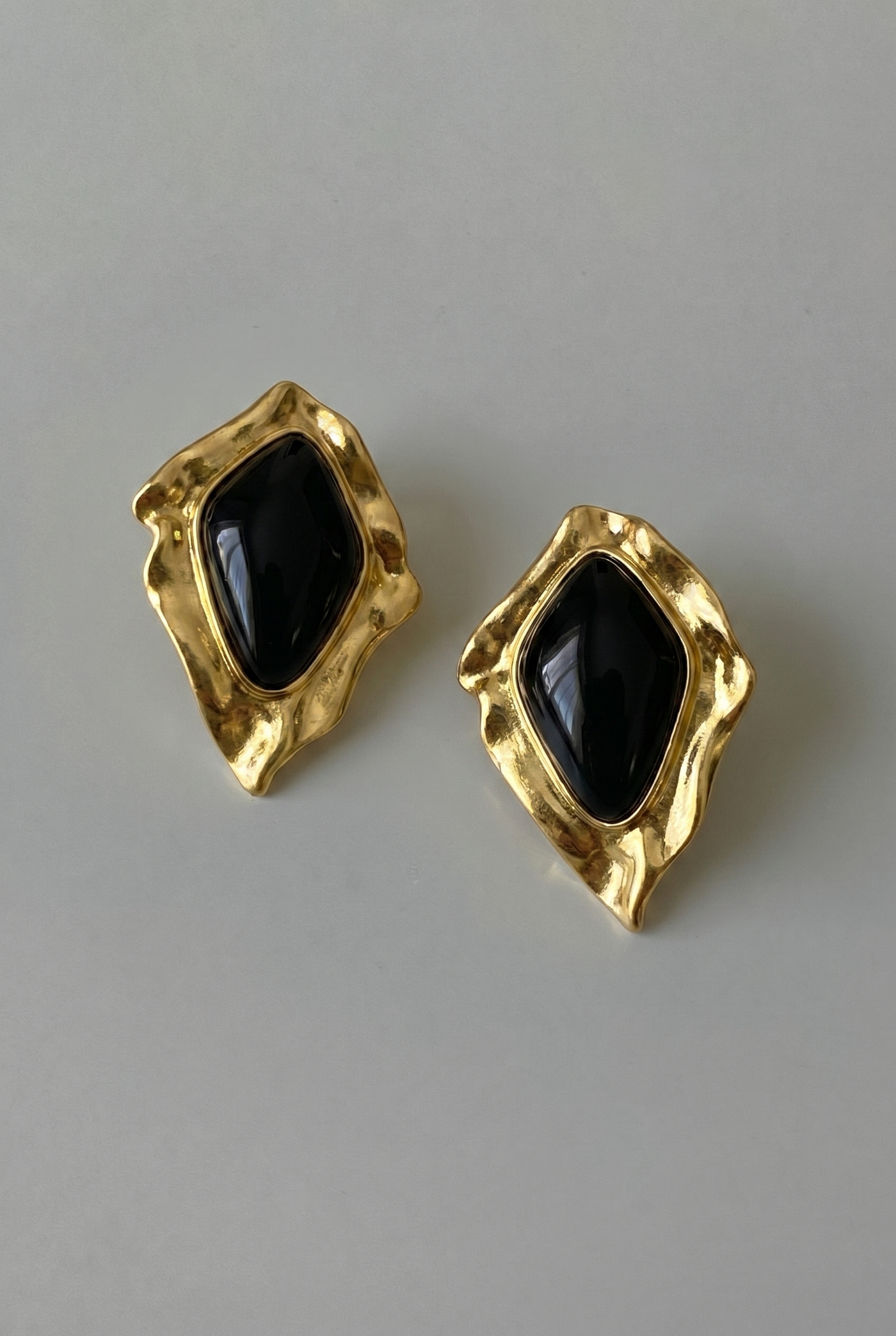 Gold earrings with black gemstones on a gray background