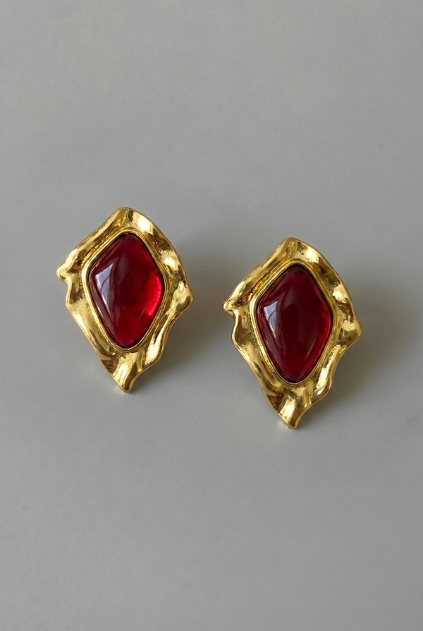 Gold earrings with red gemstones on a gray background