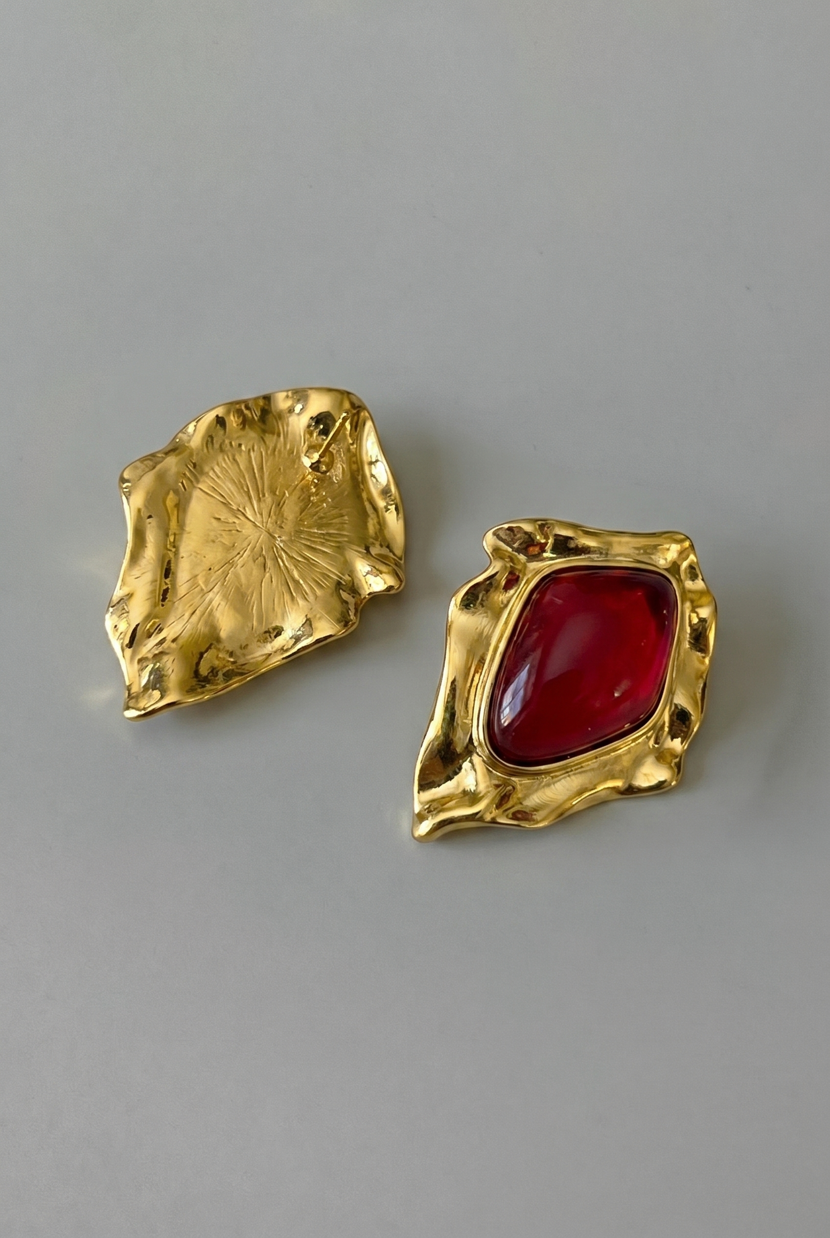 Gold earrings with a red gemstone on a gray background
