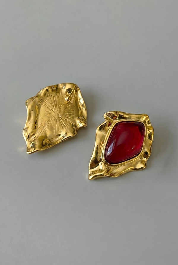 Gold earrings with a red gemstone on a gray background