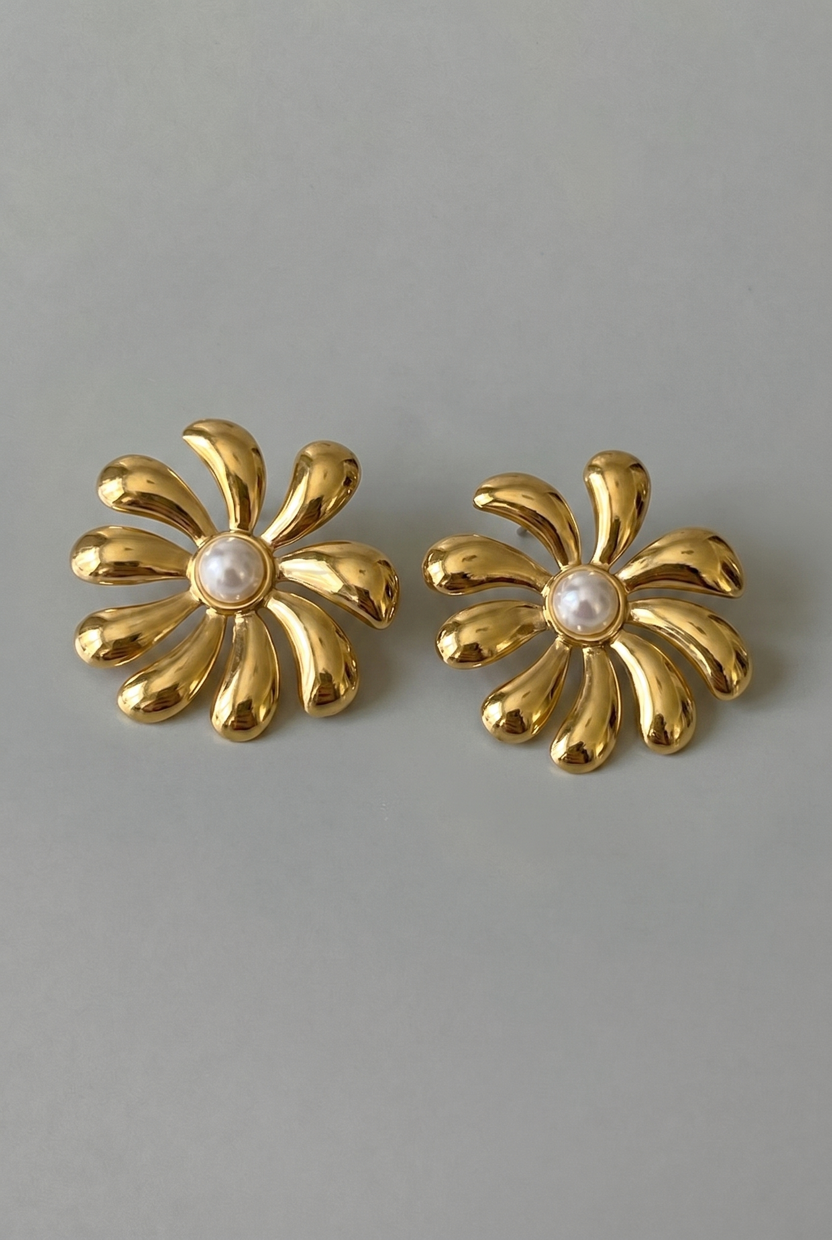 Pair of gold flower-shaped earrings with pearl centers on a gray background