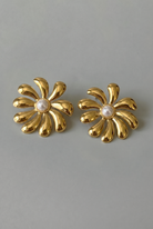 Pair of gold flower-shaped earrings with pearl centers on a gray background