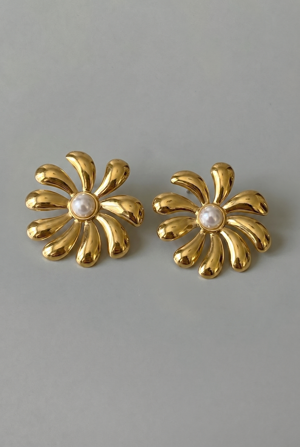 Pair of gold flower-shaped earrings with pearl centers on a gray background