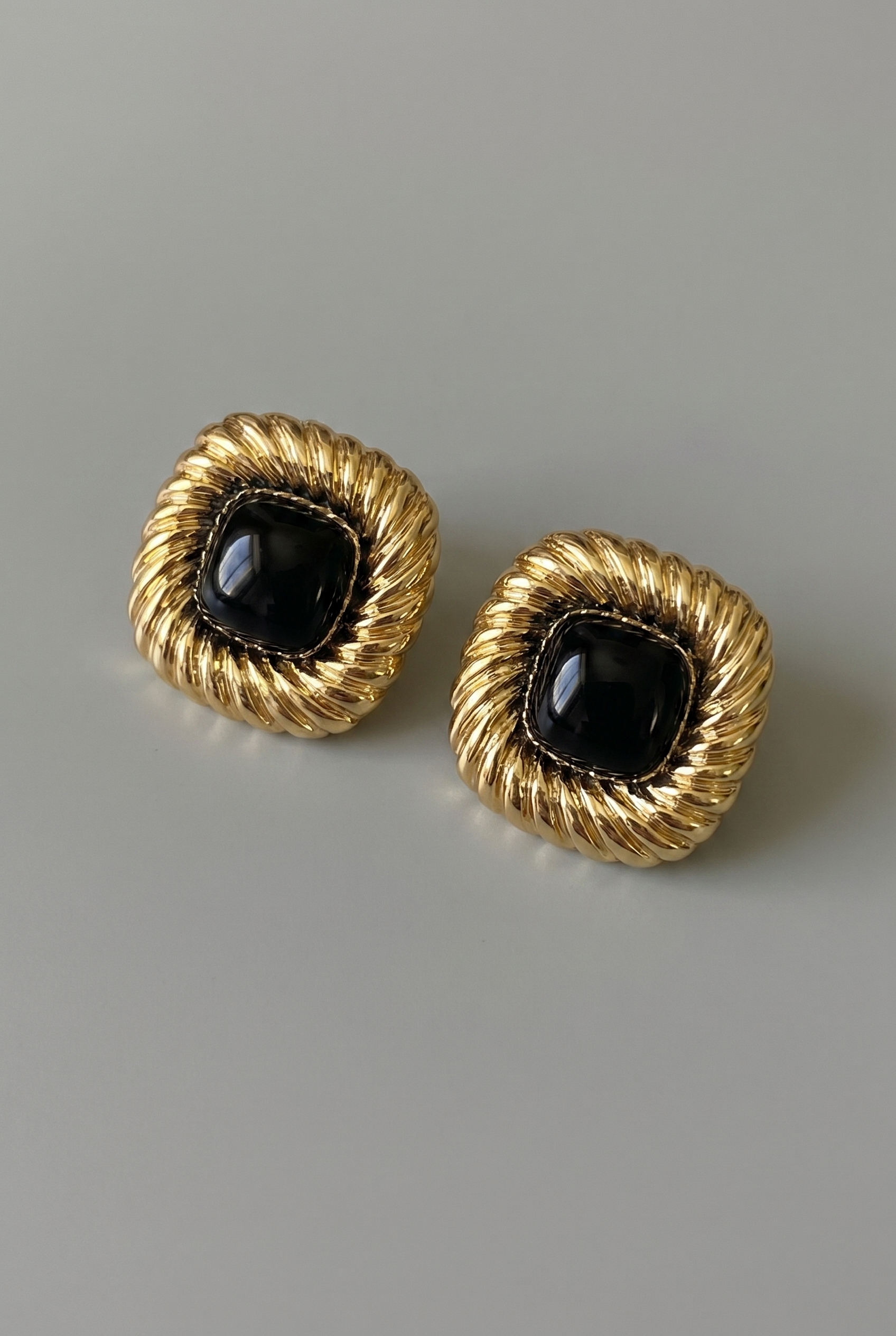 Pair of gold earrings with black stones on a gray background