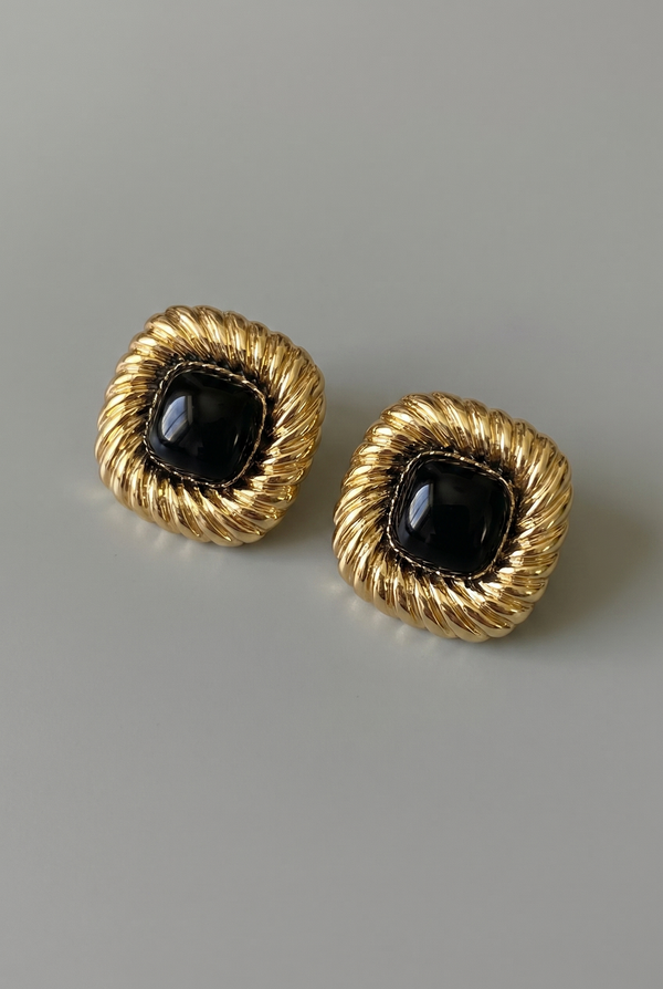 Pair of gold earrings with black stones on a gray background