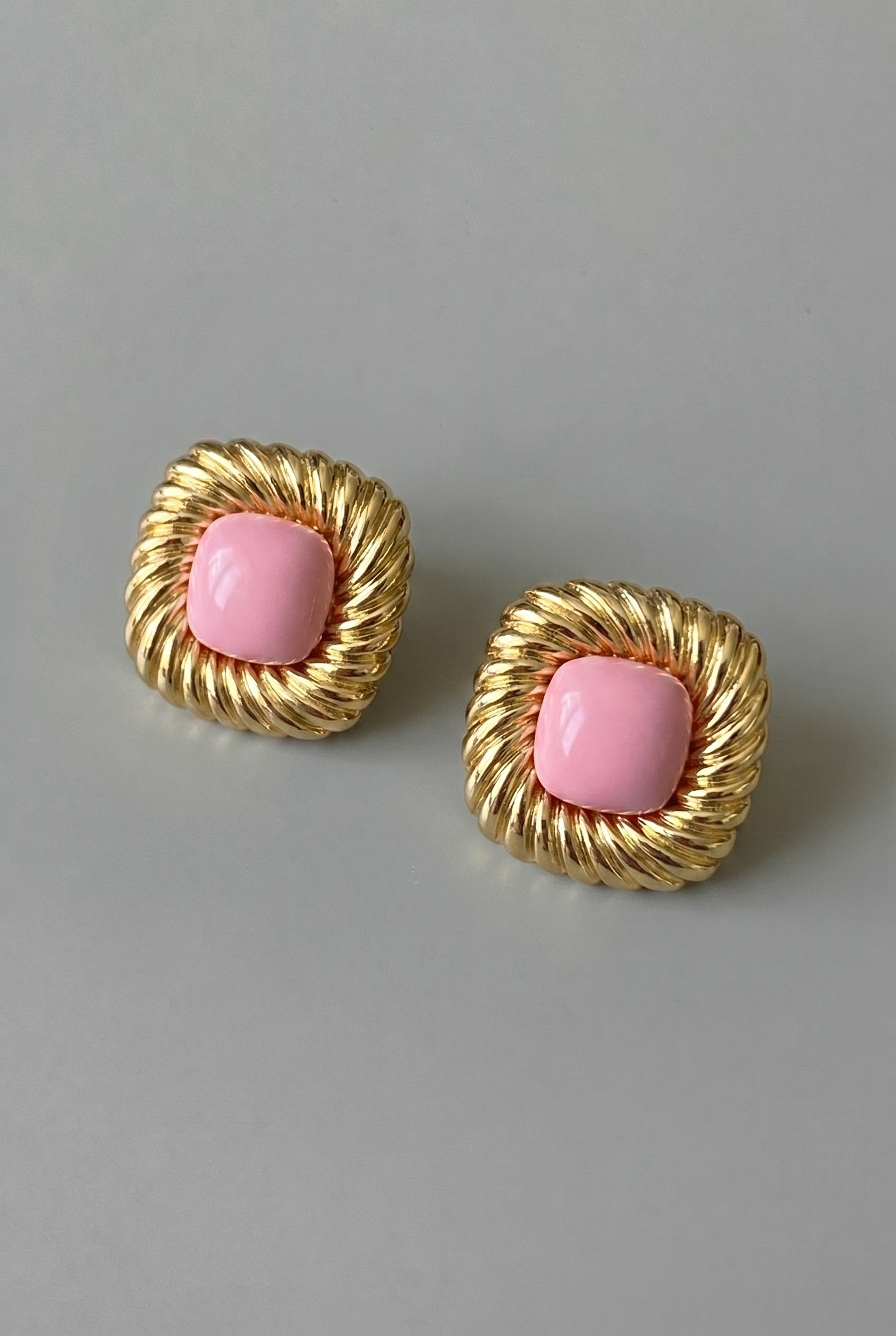 Pair of gold earrings with pink centers on a gray background