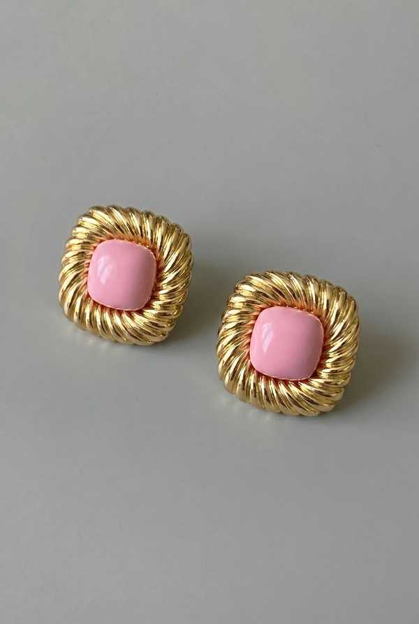Pair of gold earrings with pink centers on a gray background