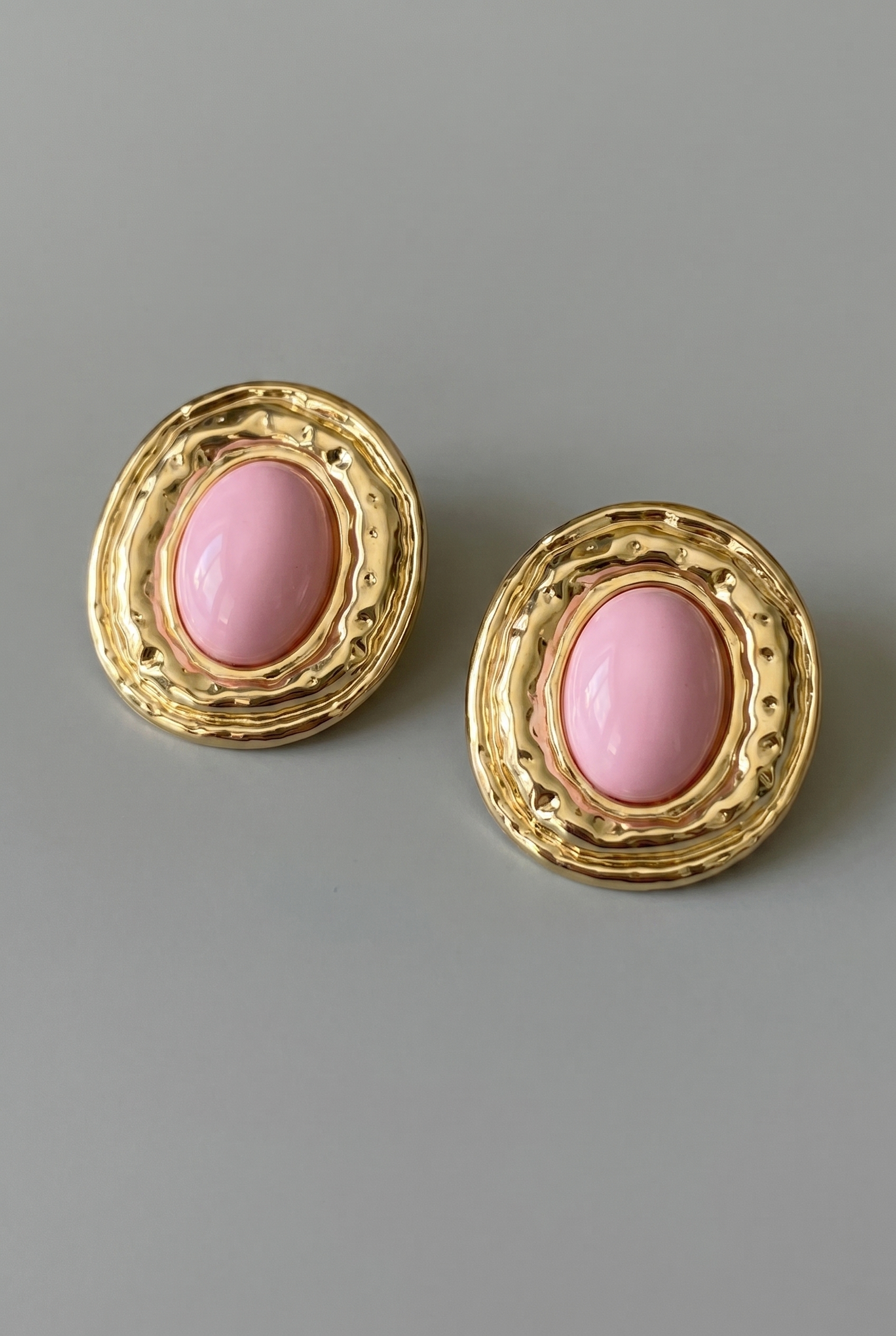 Pair of gold earrings with pink stones on a gray background