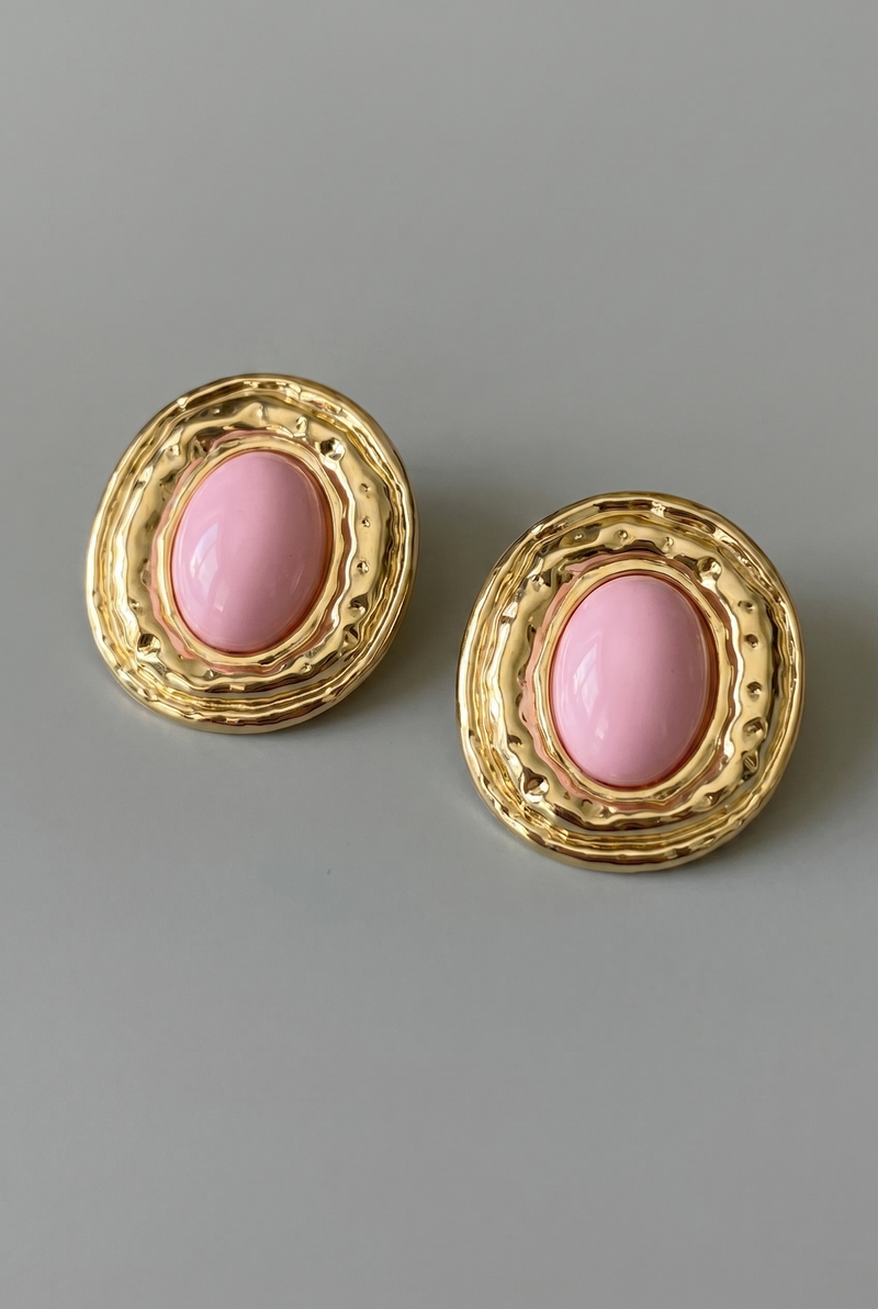 Pair of gold earrings with pink stones on a gray background
