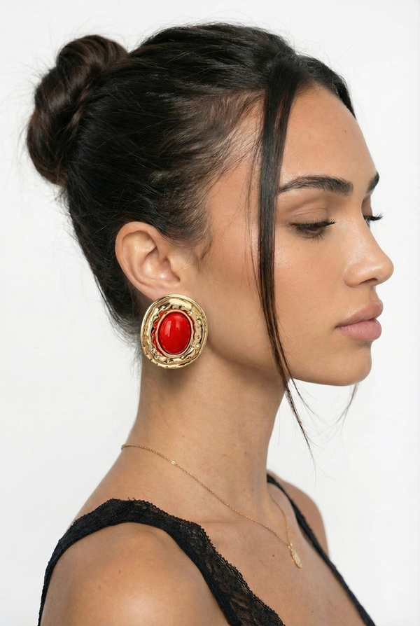 Woman wearing gold earrings with a red gemstone on a white background