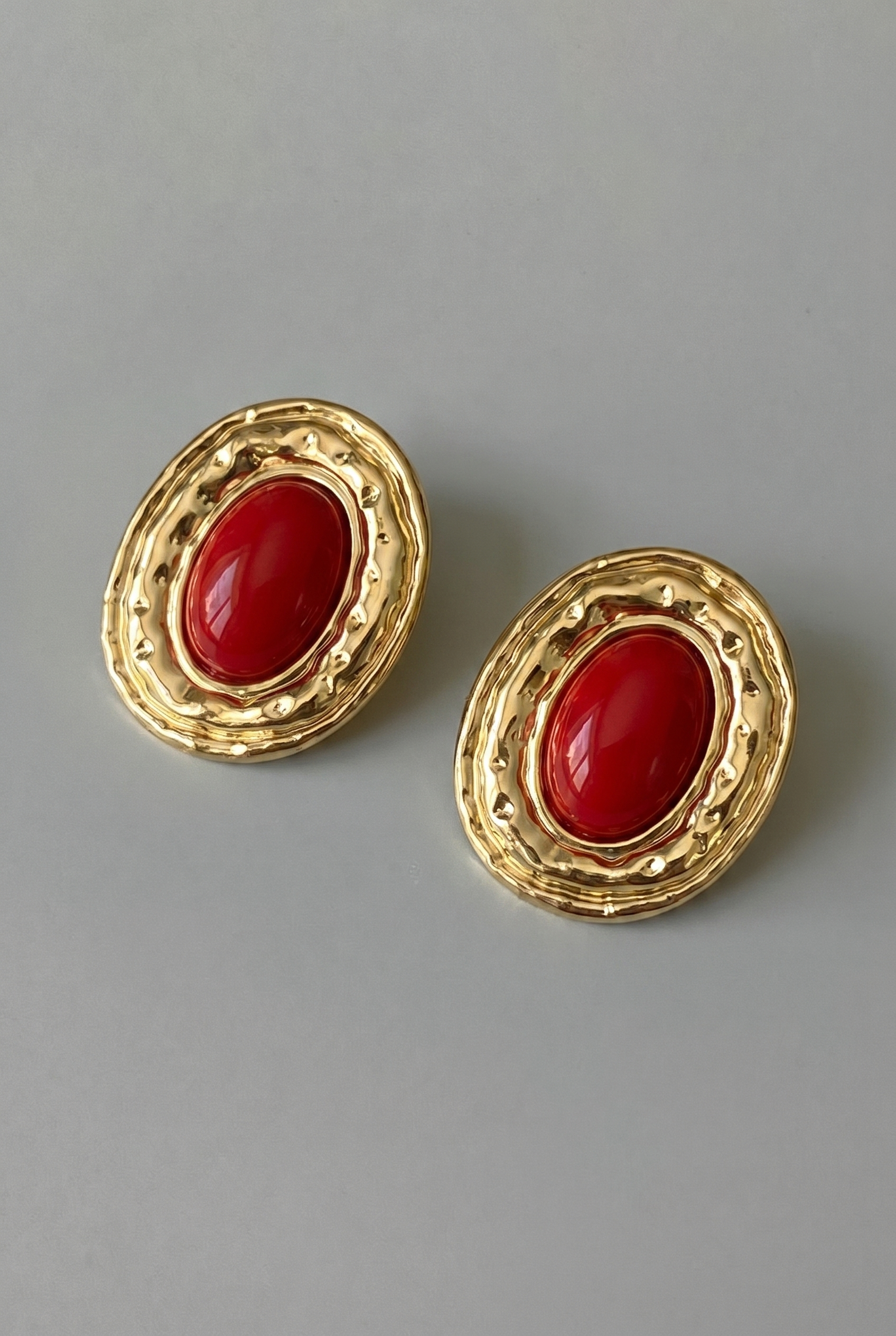 Pair of gold earrings with red stones on a gray background