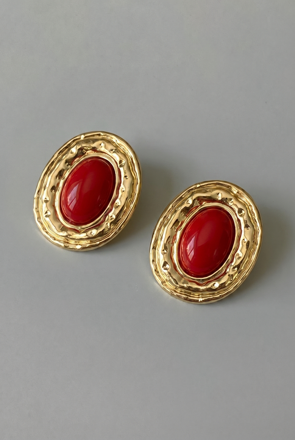 Pair of gold earrings with red stones on a gray background
