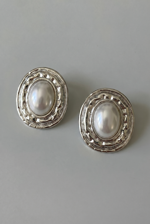 Pair of pearl earrings with silver decorative frames on a gray background