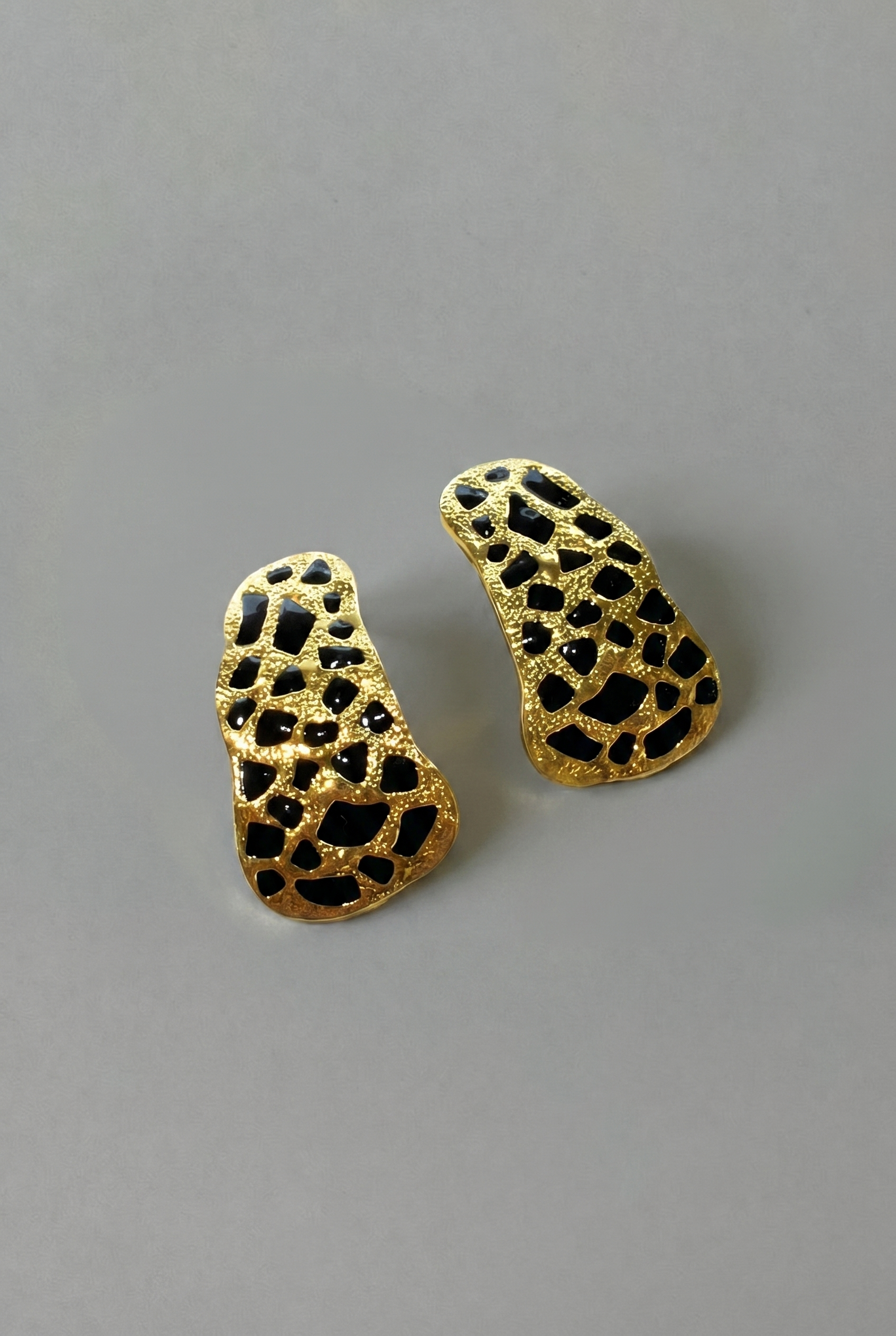 Gold and black textured earrings on a gray background