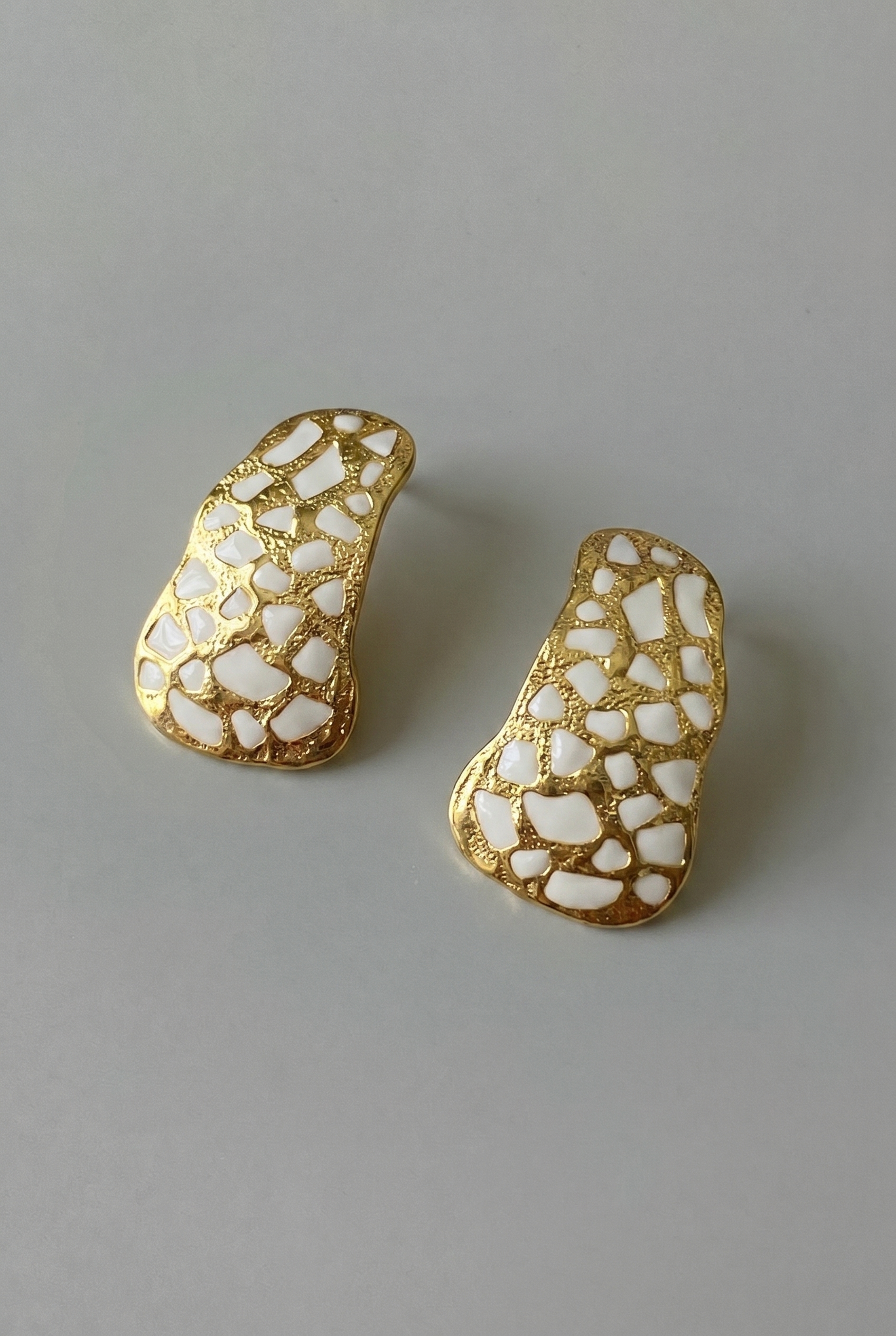 Gold and white patterned earrings on a gray background