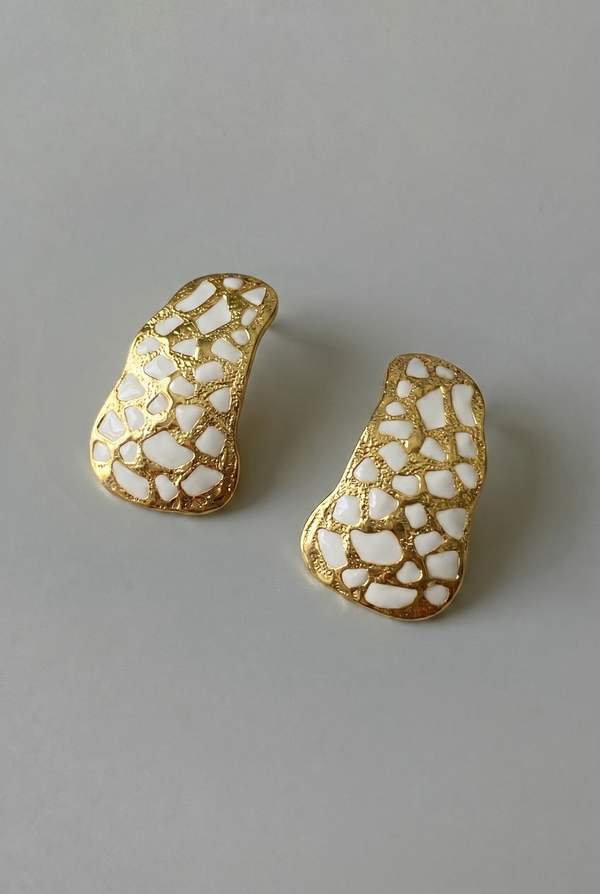 Gold and white patterned earrings on a gray background