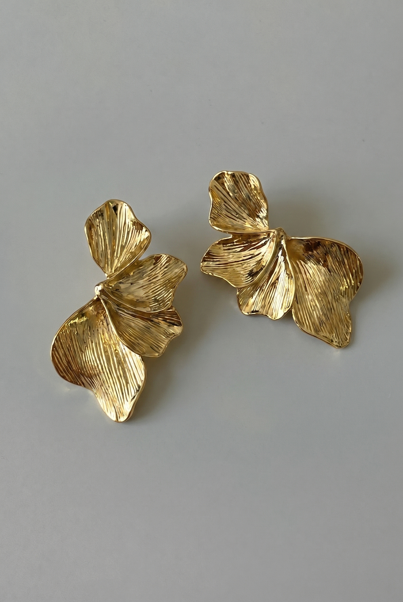 Pair of gold leaf-shaped earrings on a gray background