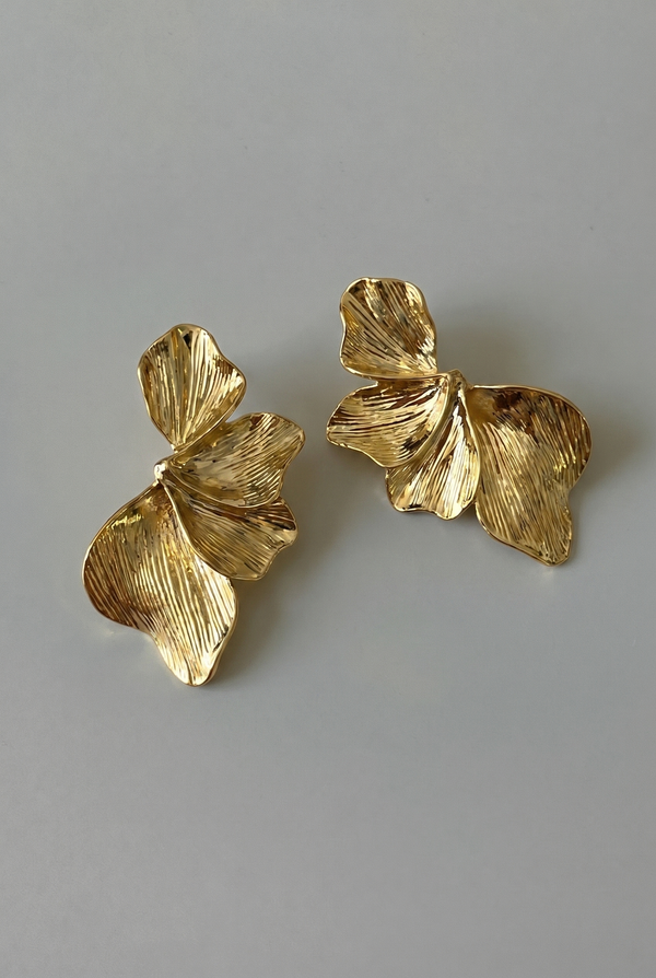Pair of gold leaf-shaped earrings on a gray background