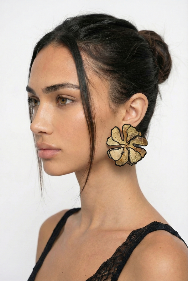 Woman wearing large gold floral earrings against a white background