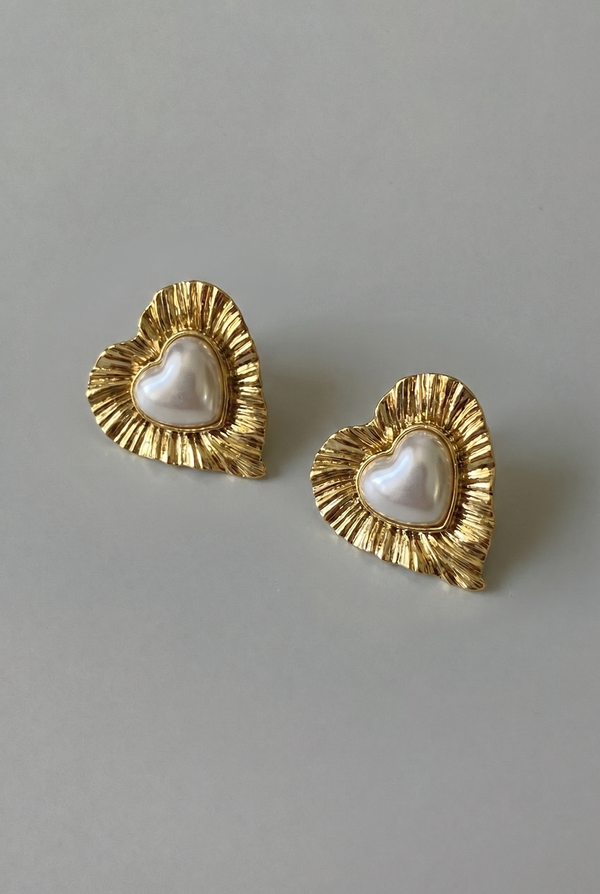 Heart-shaped earrings with gold rims and pearl centers on a gray background