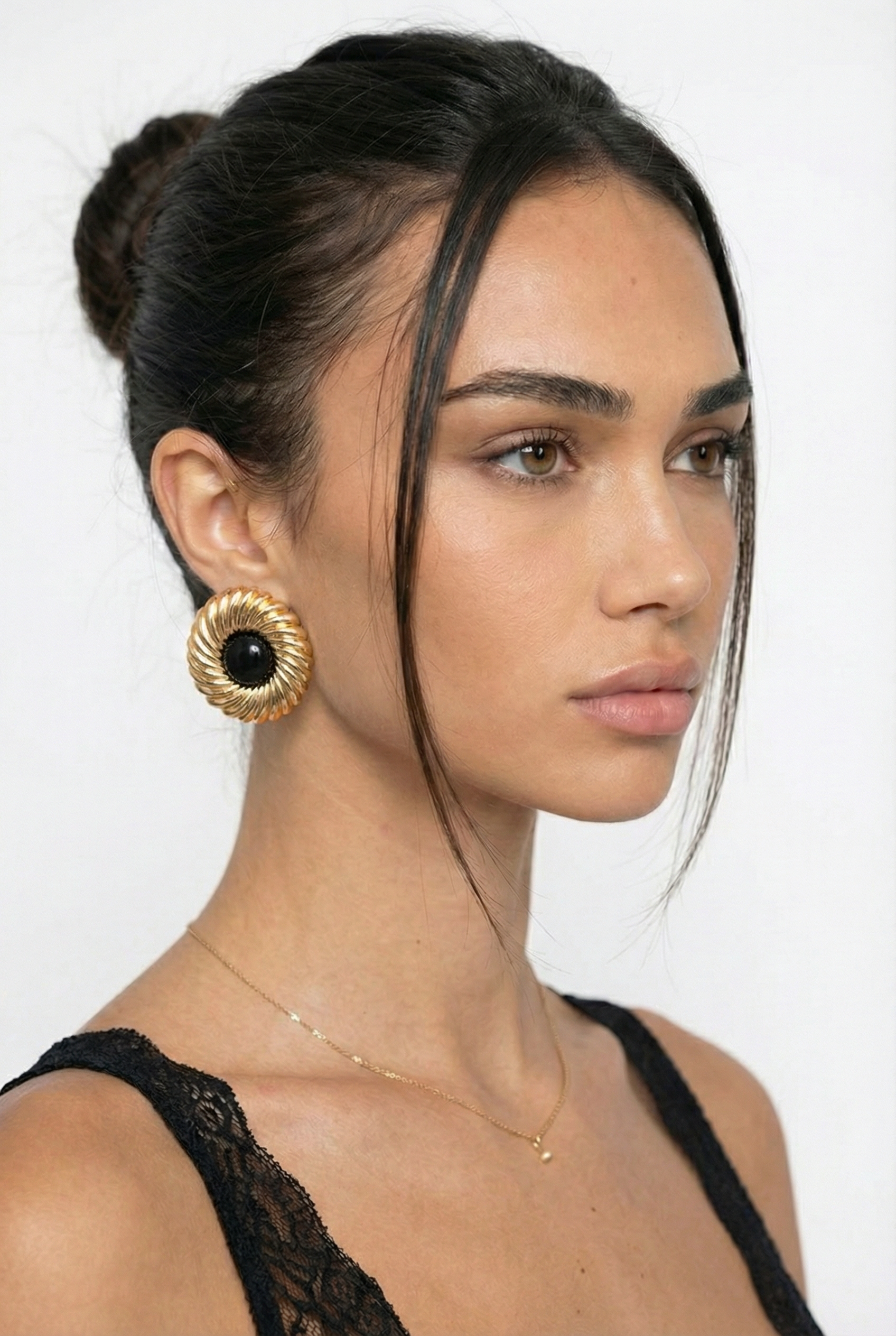 Woman wearing gold earrings and a black top against a white background