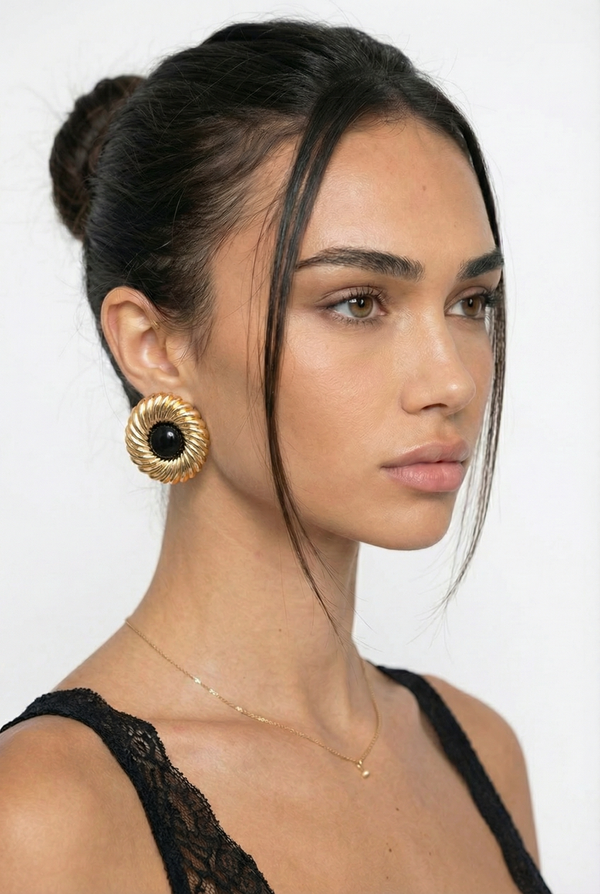 Woman wearing gold earrings and a black top against a white background