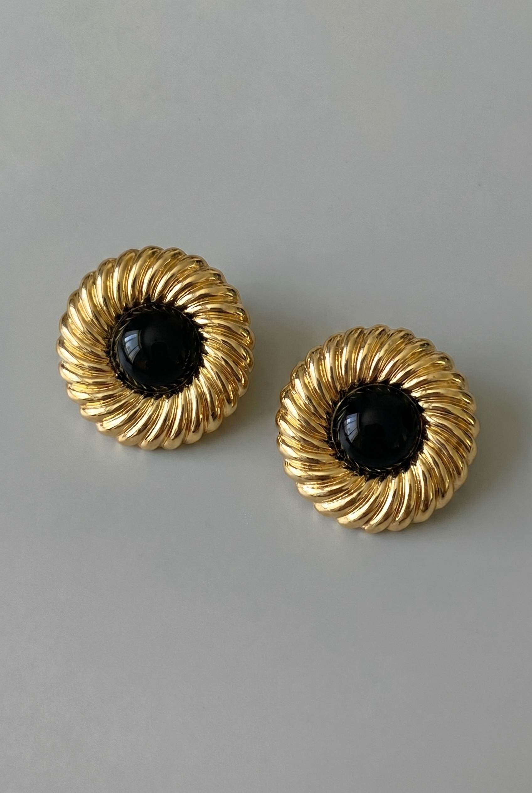 Pair of gold earrings with black centers on a gray background