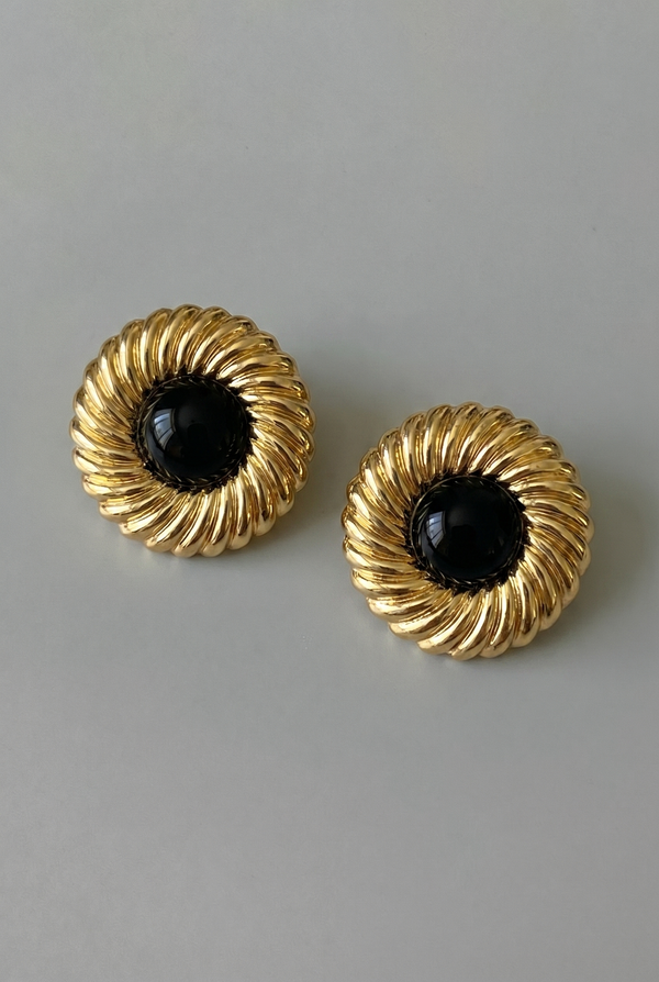 Pair of gold earrings with black centers on a gray background