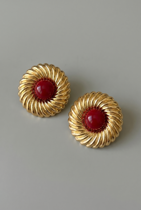 Pair of gold earrings with red centers on a gray background