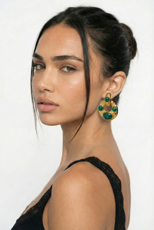 Woman wearing gold and green earrings against a white background