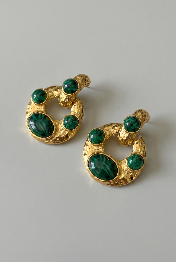 Gold earrings with green gemstones on a light gray background