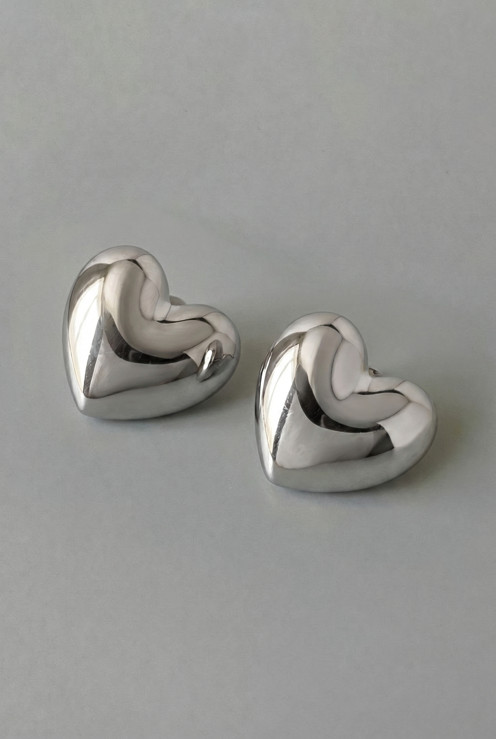 Pair of silver heart-shaped earrings on a gray background