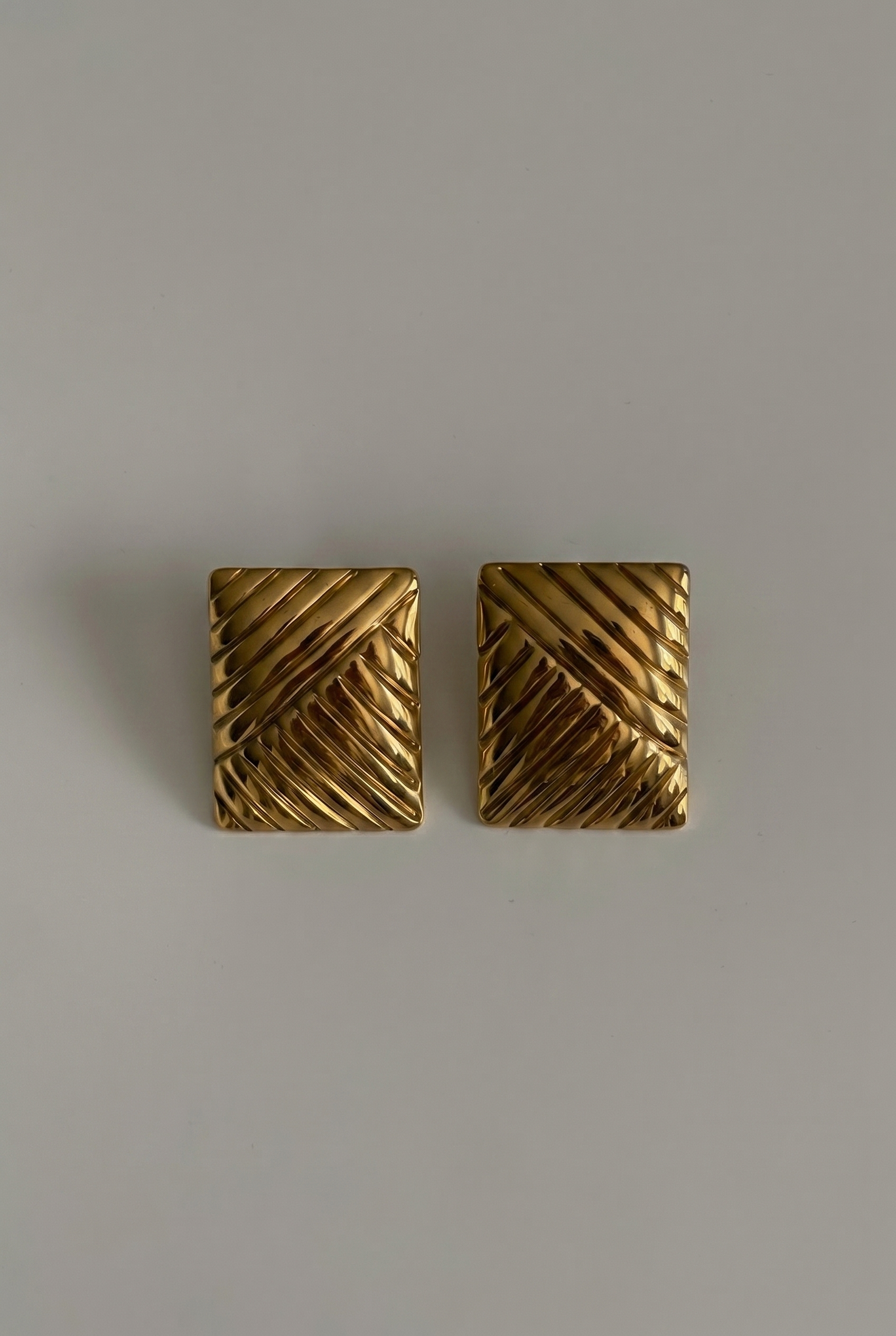 Pair of gold square earrings on a gray background