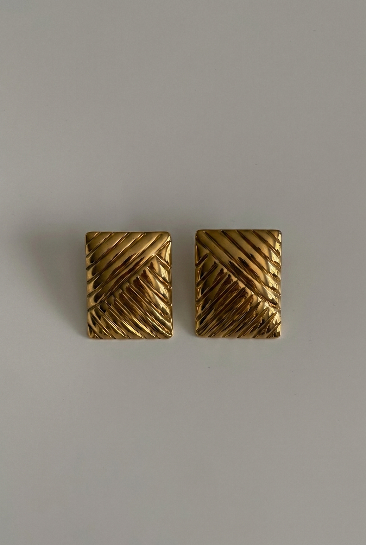 Pair of gold square earrings on a gray background