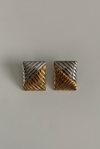 Pair of gold and silver geometric earrings on a light gray background
